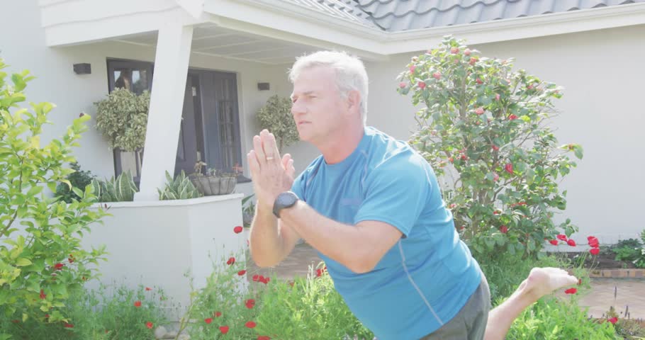 Senior man balancing on one leg front garden, smartwatch pinging and generating rising social likes. Balance, outdoor, porch, yoga, fitness, wearable, notification