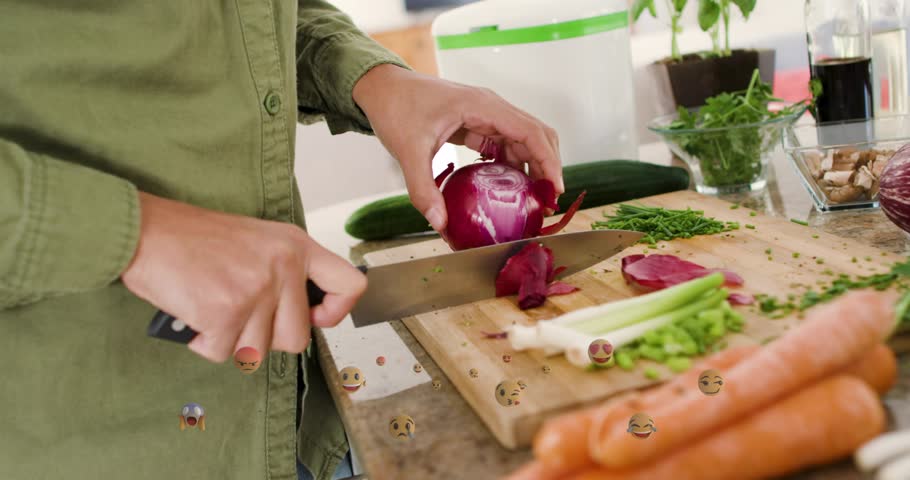 Woman steadying red onion left, guiding chef knife right, slicing, emoji overlays marking meal prep. Kitchen, vegetables, chopping, homecooking, produce, herbs, countertop