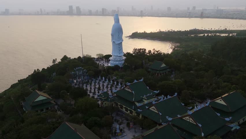Aerial sunset Panoramic over the distant Da Nang city skyline and coastline, viewed from the Son Tra Peninsula as city lights begin to glow