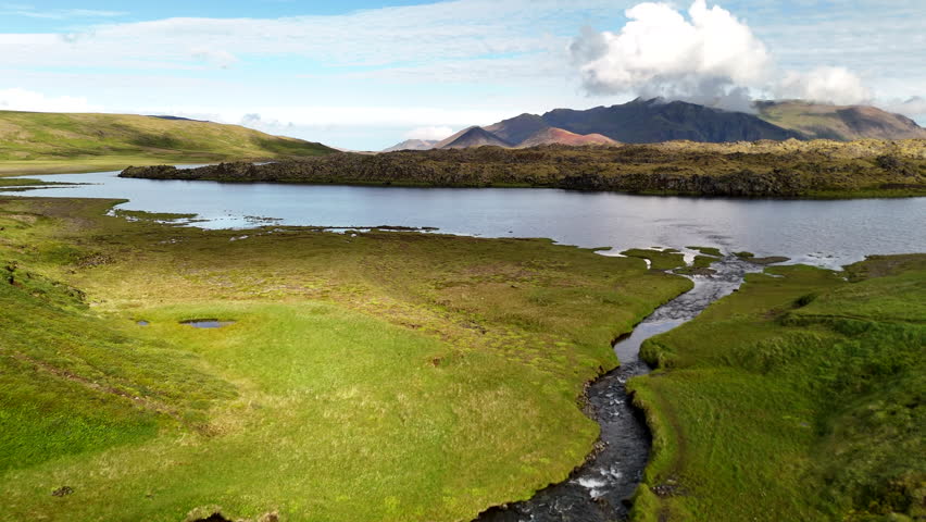 Aerial view of Selvallafoss and Selvallavatn on the Snæfellsnes Peninsula showing calm lake water mossy lava fields and distant mountains under bright clouds in a pristine Icelandic volcanic landscape