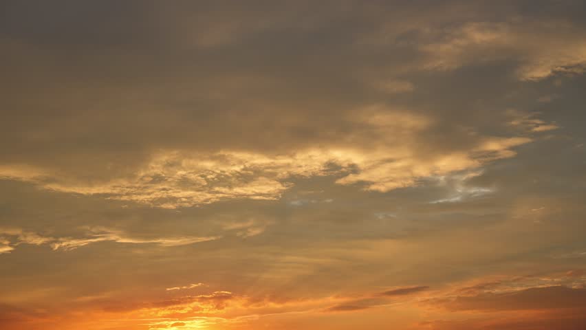 A sunset sky timelapse showcasing glowing altocumulus and stratocumulus clouds ignited in deep orange and gold, forming dramatic layered textures that highlight the shifting evening light. Time-lapse.