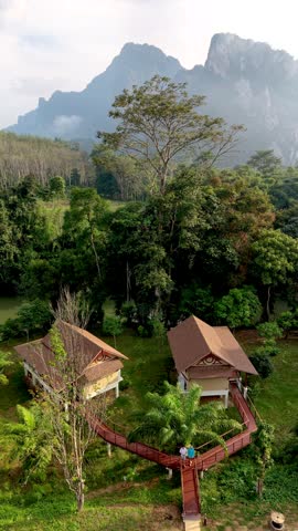 Experience the serene beauty of Khao Sok, Thailand, where traditional bungalows nestle among lush greenery, surrounded by majestic mountains.