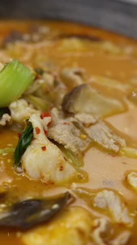 Closeup of chopsticks lifting pork and vegetables from bubbling spicy hotpot in warm lighting