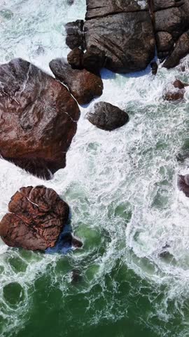 aerial top-down view of ocean waves crashing against large rocks on a shoreline