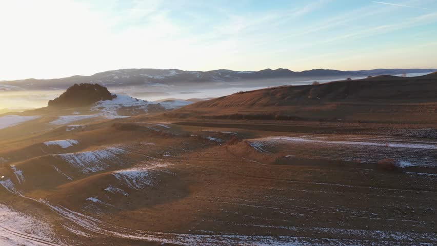 Aerial view of sunset lights over frosty countryside hills by drone