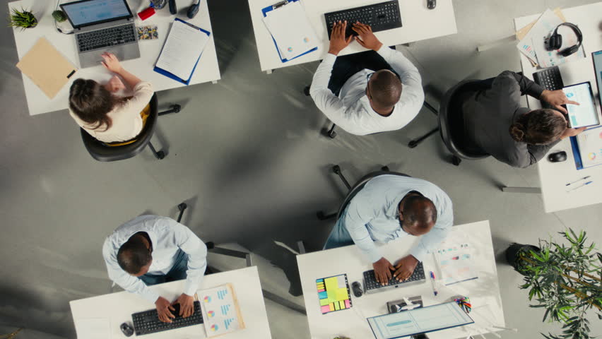 Collaborative team in company office sharing project files via cloud integration, digital ecosystem HUD icons. Aerial view of business colleagues syncing documents via online network on remote server