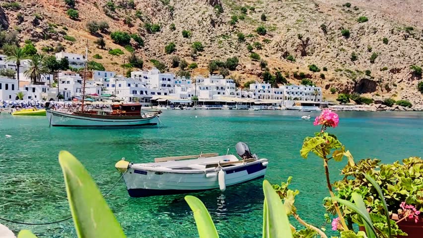 Aerial view of Loutro Village, Crete, with colorful boats, crystal-clear turquoise water, and charming whitewashed buildings, highlighting a serene Mediterranean paradise.