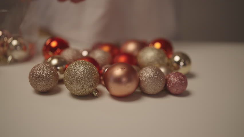 Closeup hands of unrecognizable person arranging vibrant collection of Christmas ornaments, including glittery gold, matte red and rose gold baubles, preparing for festive holiday decorating.