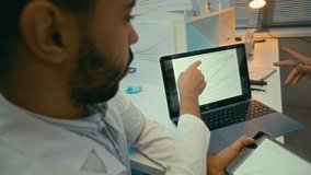 Handheld shot of multiethnic team of scientists in lab coats sitting in modern laboratory office and discussing chemical reaction rates on tablet and laptop screens - Powered by Shutterstock - Get 15% off with code: PIKWIZARD15