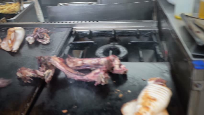 Close up of a chef grilling squid and meat on a commercial griddle