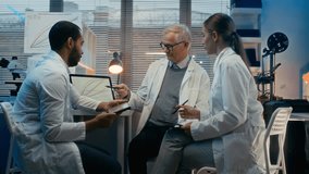 Medium long shot of senior Caucasian male scientist teaching young multiethnic assistants or students in modern laboratory office, showing chemical reaction rates on laptop screen - Powered by Shutterstock - Get 15% off with code: PIKWIZARD15