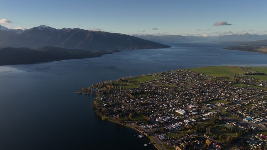Scenic 4K aerial drone footage of Te Anau town on the shores of Lake Te Anau, Fiordland. Majestic sunset view of the township, deep blue water, and snow-capped mountains in New Zealand