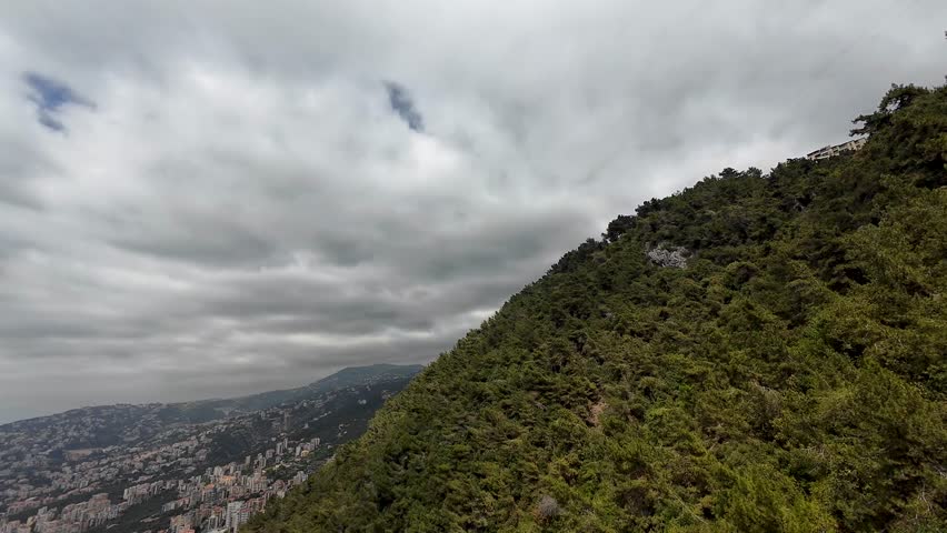Cable car traveling over a forested hillside near a city with a blue sky. Lebanon