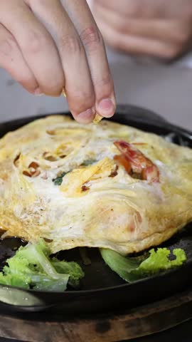 Close-up of hand squeezing lime over Thai omelette on sizzling plate at night market