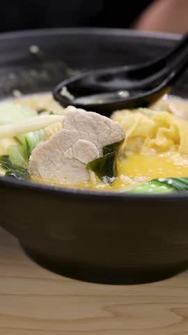 Close-up of hot chicken noodle soup dumpling lifted and dipped into vibrant spicy herb sauce