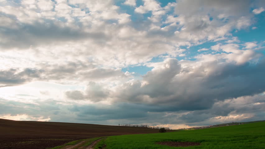 White puffy clouds rolling above fields, time lapse.