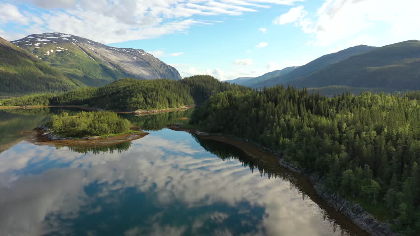 Drone view of calm lake reflecting clouds and mountains.