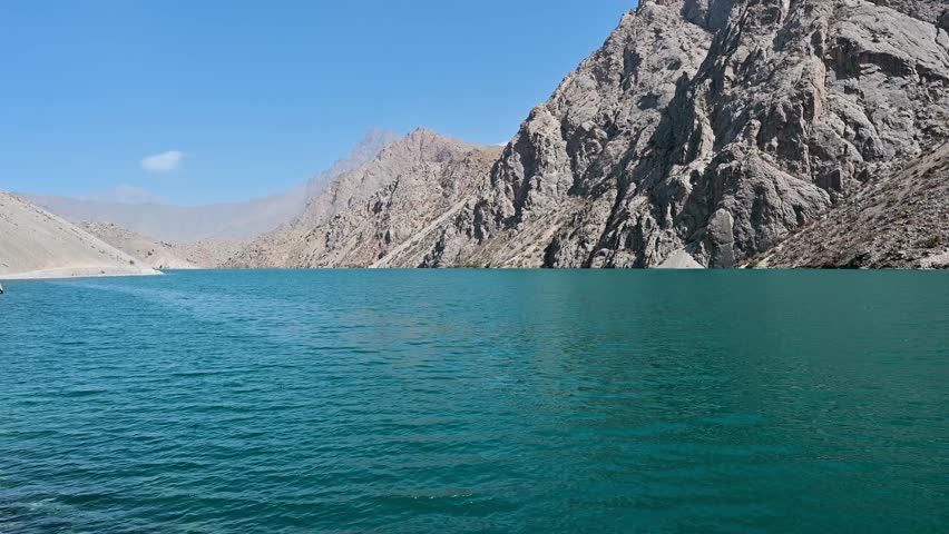 A slow motion view of Hazorchashma Lake, the seventh lake of the Seven Lakes in the Fann Mountains near Panjakent, Tajikistan, showing calm blue water and rocky mountain surroundings.