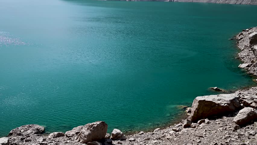 A wide view of Marguzor Lake, the sixth lake of the Seven Lakes in the Fann Mountains near Panjakent, Tajikistan, with deep blue water, steep rocky hillsides, and clear mountain daylight.