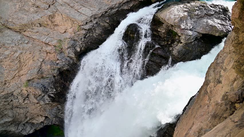 A panning view of Iskanderdarya Waterfall near Iskanderkul in the Fann Mountains of Tajikistan, with fast flowing water cutting through rocky cliffs in a remote Central Asia setting.