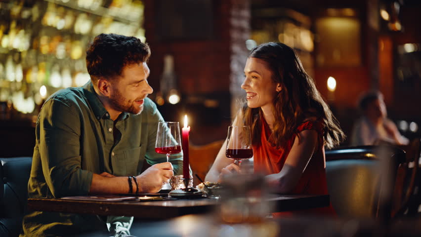 Lovely pair toasting glasses celebrating anniversary in luxury restaurant closeup. Smiling affectionate couple enjoying romantic dinner drinking red wine. Smiling woman man talking relaxing together.