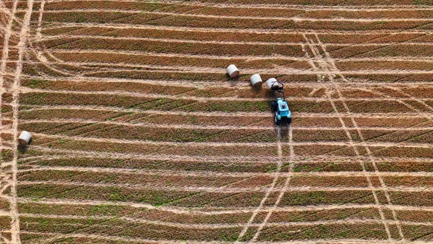 Drone video of tractor using front loader to collect hay bales from field