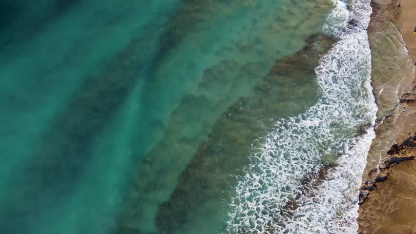 A view of waves washing over sand and scattered rocks along the Lagos coast of Portugal, showing shoreline textures and shallow turquoise water.