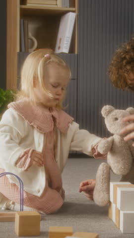 Vertical side view shot of teen brother and little little sister playing together sitting on floor with wooden blocks and toys