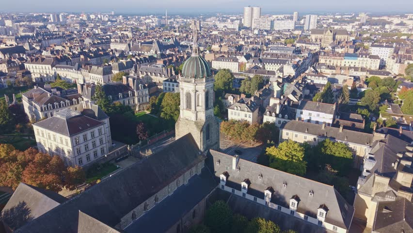 High-angle establishing shot showcasing the dome and tower of the historic Notre-Dame-en-Saint-Melaine Church dominating the densely packed urban architecture of the Rennes cityscape.