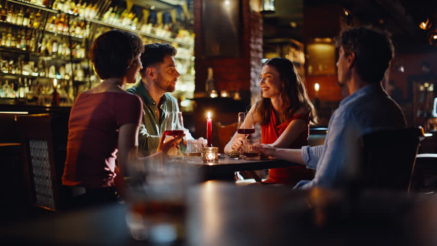 Two couples date night in luxury restaurant. Group happy friends enjoying pleasant communication in modern bar interior. Relaxed men women talking laughing at weekend hangout. Friendship concept.
