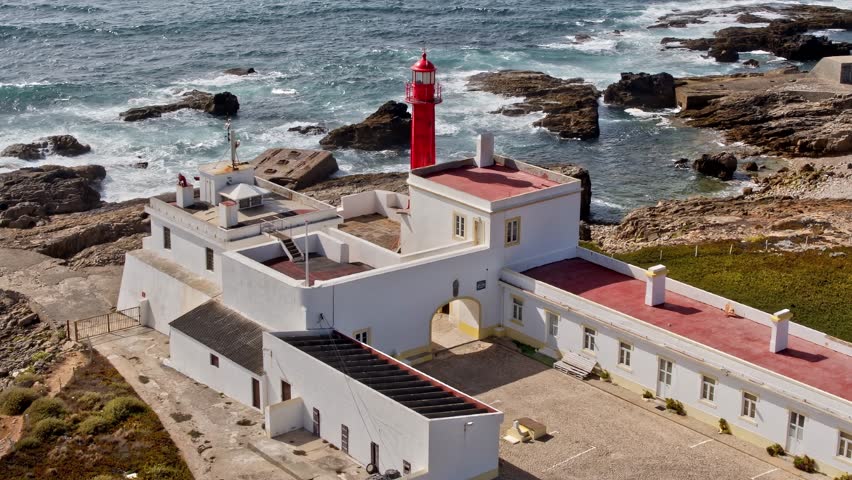 A lighthouse located on a rocky shoreline in Portugal. Waves crash against the rocks while the lighthouse stands tall against the sky.