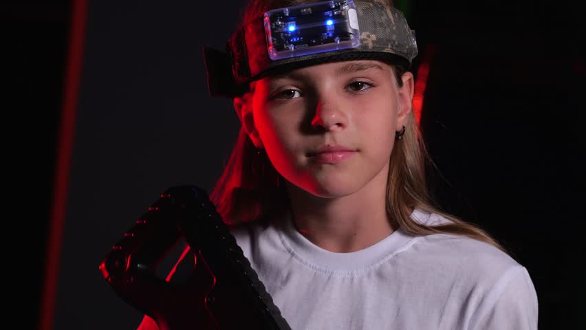 Portrait of a girl with a laser tag marker on her head and a laser tag gun in a dark room. The concept of active tactical games for teenagers.