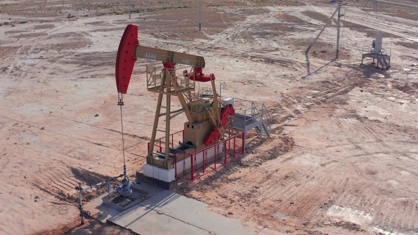 Single oil pumpjack with red details working in isolated desert oilfield. Drone view sandy landscape, dry soil, sparse vegetation, and sense of industrial isolation in energy extraction site.