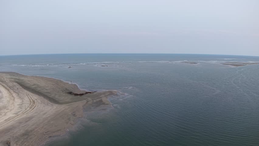 Aerial drone footage of Charleston, South Carolina capturing a sandy peninsula extending into calm blue water, with a wide river or bay and a distant horizon on a hazy day.