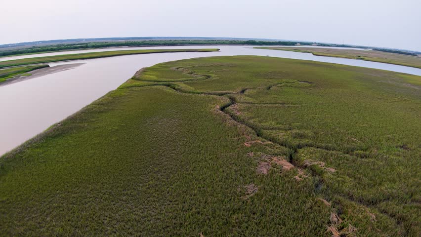 Drone footage capturing Charleston, South Carolina’s marshland peninsula with a wide river on one side and winding tidal creek on the other at dusk.