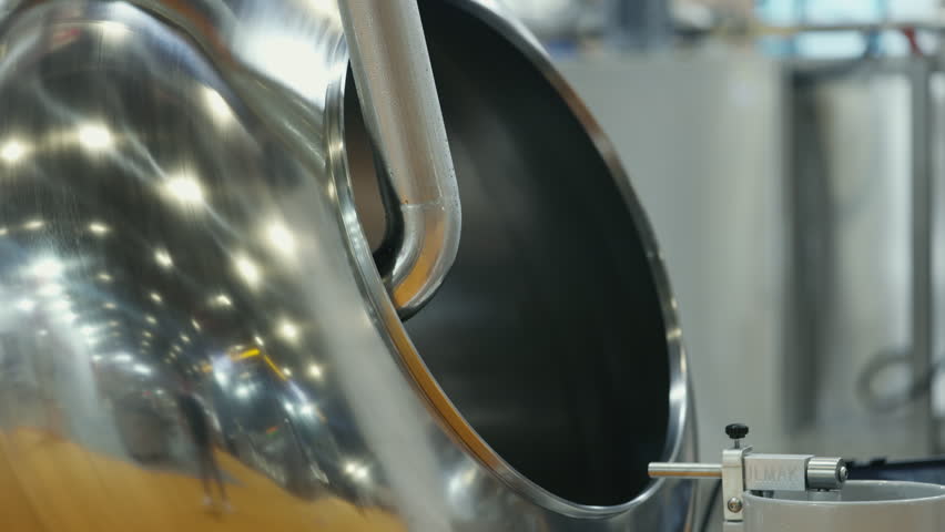 Close-up view of a polished stainless steel mixing drum used in food or chemical production. Smooth reflective metal surface with industrial details in a modern manufacturing environment.