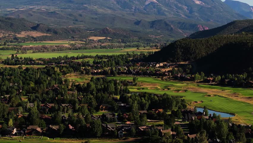 Lush valley spreads below Mount Sopris with rich greens contrasting the rugged Colorado summit, aerial tilt up establishing