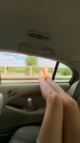 Legs are comfortably positioned on car seat, showcasing a beautiful landscape through the open window, with a smooth pan capturing the tranquil journey