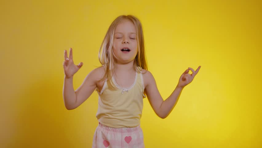 Joyful young girl with long blonde hair celebrating or dancing against a vibrant, sunny yellow backdrop, wearing a light yellow tank top and patterned shorts. Child raising both fists enthusiastically