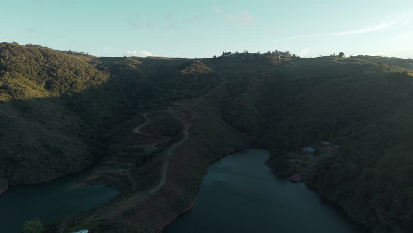 Drone shot over Lago Calima in Valle del Cauca captures serene water and lush hills under golden light, offering a breathtaking aerial perspective of Colombian natural beauty.
