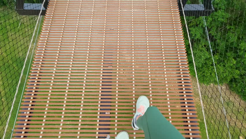 Overhead view of a single female walking on a suspension bridge high in the sky. The bridge connects two mountains with views of the valley below. Located in Northern Michigan, USA. 
