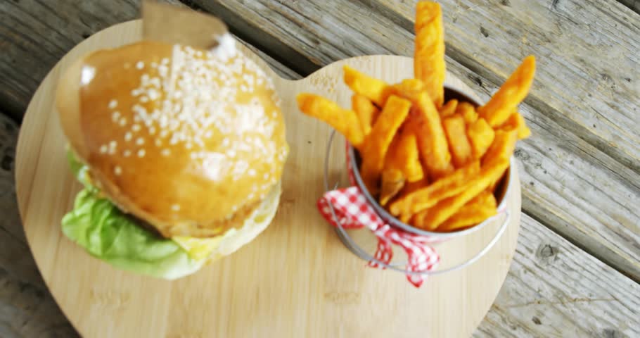 Left overlays appearing and drifting over still burger and fries as camera panning right for promo. Rustic, wooden, servingboard, sandwich, potato, gingham, weathered