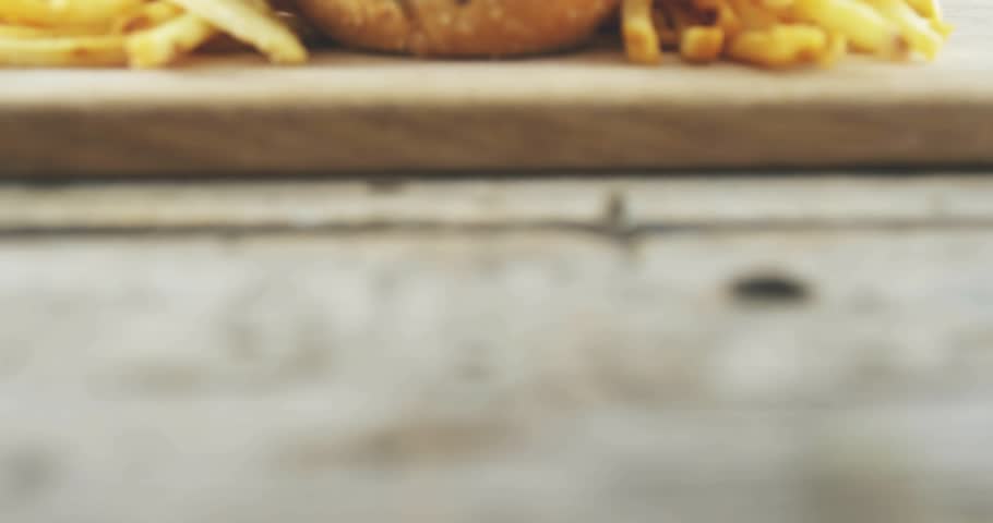 Camera pulling back revealing three seeded sliders, fries and floating icons counting up for promo. Burgers, rustic, tabletop, cuttingboard, sesame, toothpick, promotion