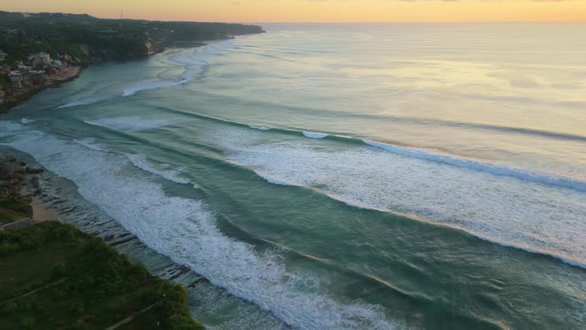 Drone footage showcasing rhythmic waves and sunset hues along Canggu, Bali's stunning coastline, capturing the serene ambiance and majestic oceanic vistas from a high-altitude perspective.