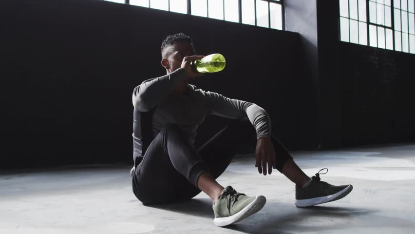 Animated graphic shifting into VIBES, man grabbing green bottle, drinking then pouring for fitness. Industrial, studio, backlit, silhouette, warehouse, athletic, glitch
