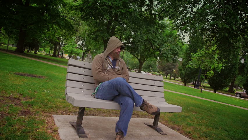 A sad man sits alone on a park bench.
