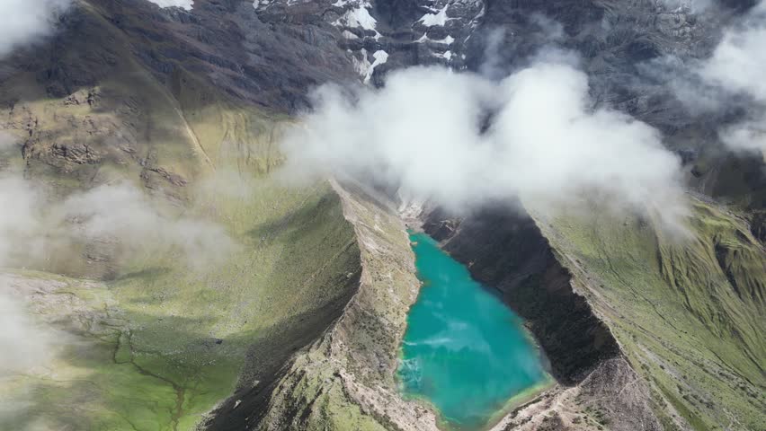 Aerial footage of Humantay Lake, Andes Peru, showcasing mirror-like cloud reflections in turquoise glacial water under sunshine.