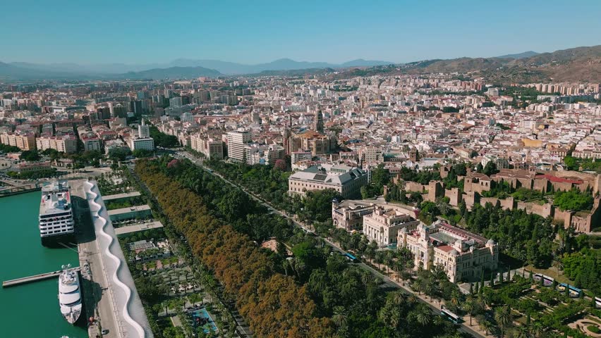 Aerial shot over Málaga’s waterfront and Parque de Málaga, Spain, moving toward the Cathedral and historic city center under bright clear skies.