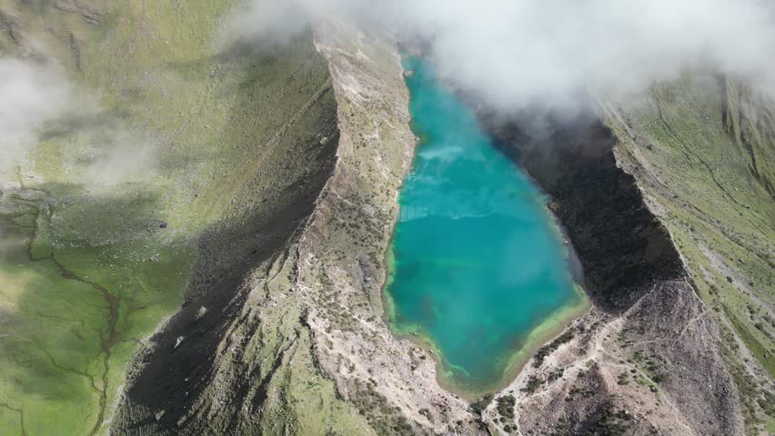 Drone footage of Humantay Lake, Peru, capturing dynamic cloud reflections across calm glacial water in sunny conditions.