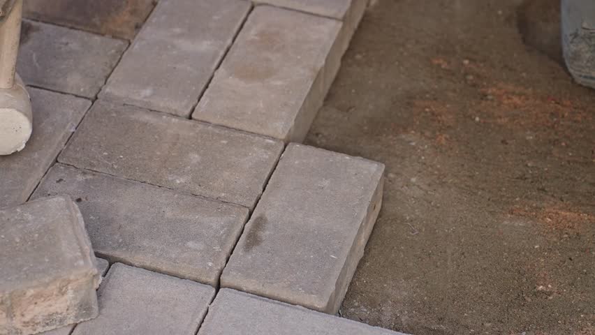Top view close-up of worker laying paving stones with a mallet, demonstrating hard manual labor and step by step construction tutorial.